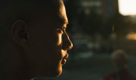 Portrait de profil d'un homme baigné dans la lumière dorée d'une fin de journée. L'arrière plan est flou mais laisse deviner la ville de Marseille. 