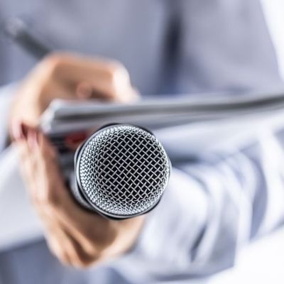 un journaliste tient un micro tout en ecrivant sur un cahier, lors d'une conference de presse