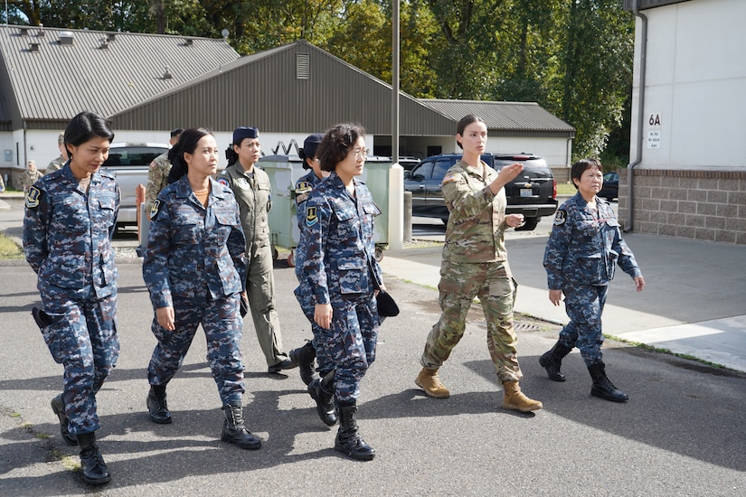 A guardsman leads a group of female officers through the street in a military base during the day.