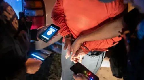 ICE Officers Make An Arrest While Holding Phone and Using a Mobile App with Facial Recognition Screen Showing