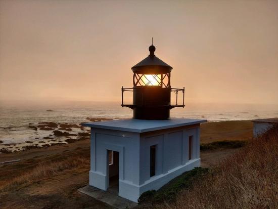 Lighthouse with white base glowing in fog. 