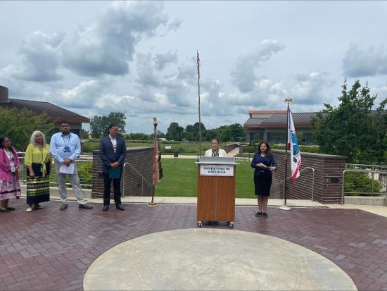 Secretary Haaland speaks at a podium with Department and White House leaders and Tribal representatives standing off to the side. 