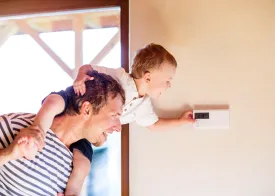 Son riding on Dad's shoulders tries to reach a wall thermostat