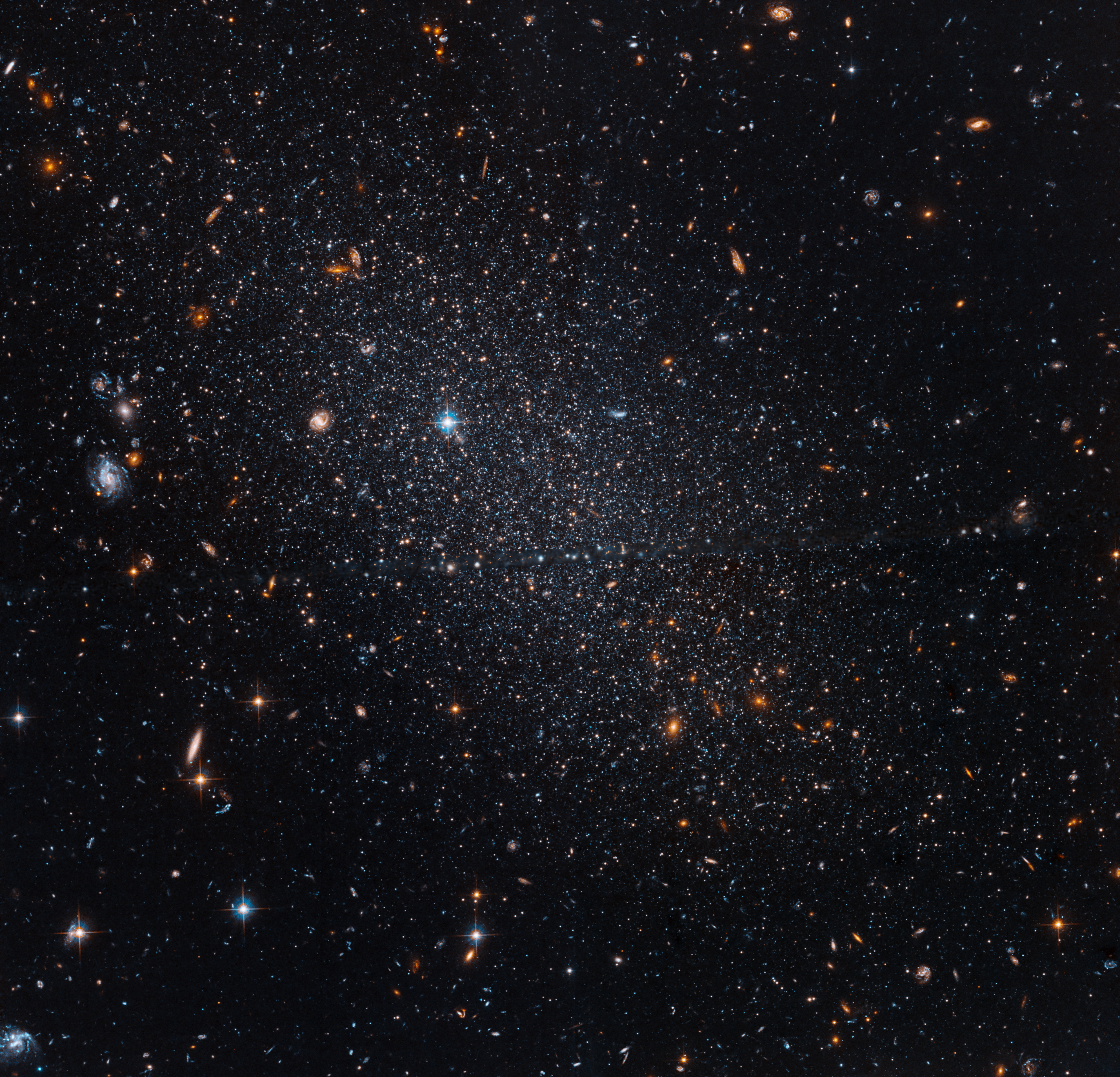 More closely concentrated near the center, several stars shine against black space along with a few distant galaxies.