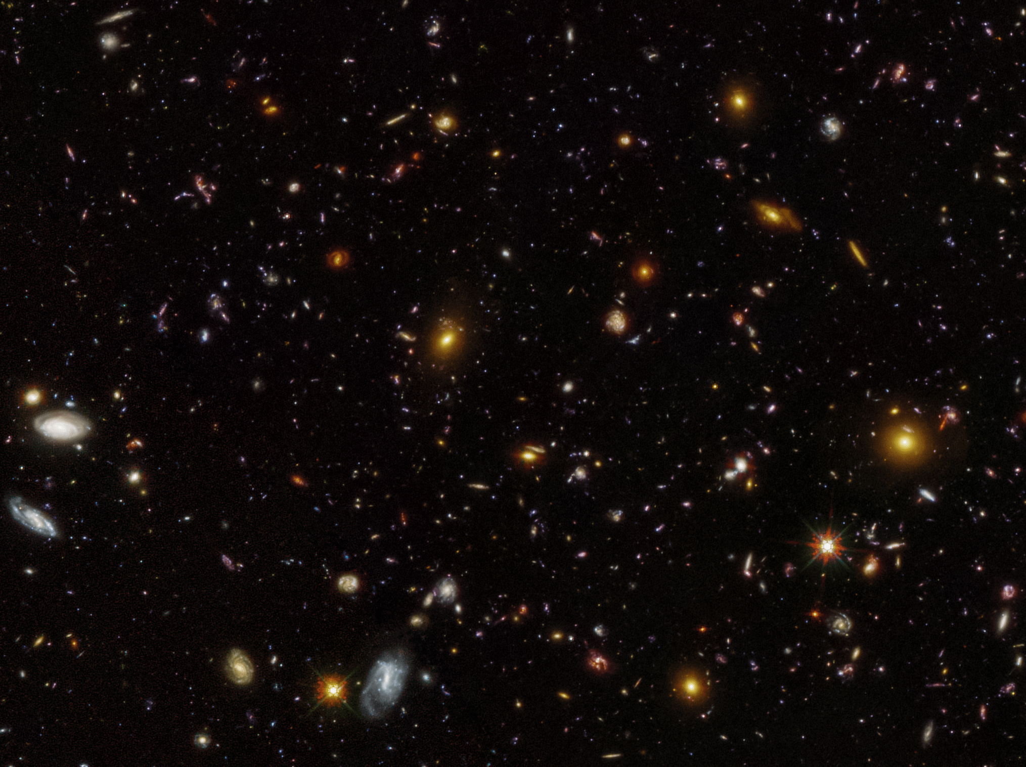 A field of galaxies of various shapes, sizes, colors, and types against a black backgrouns.