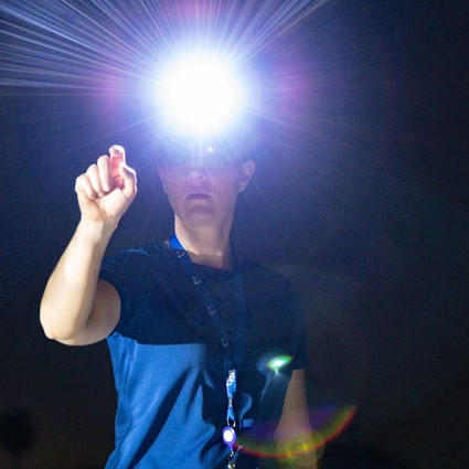 Person pointing with finger forward, with helmet and light shining from helmet.