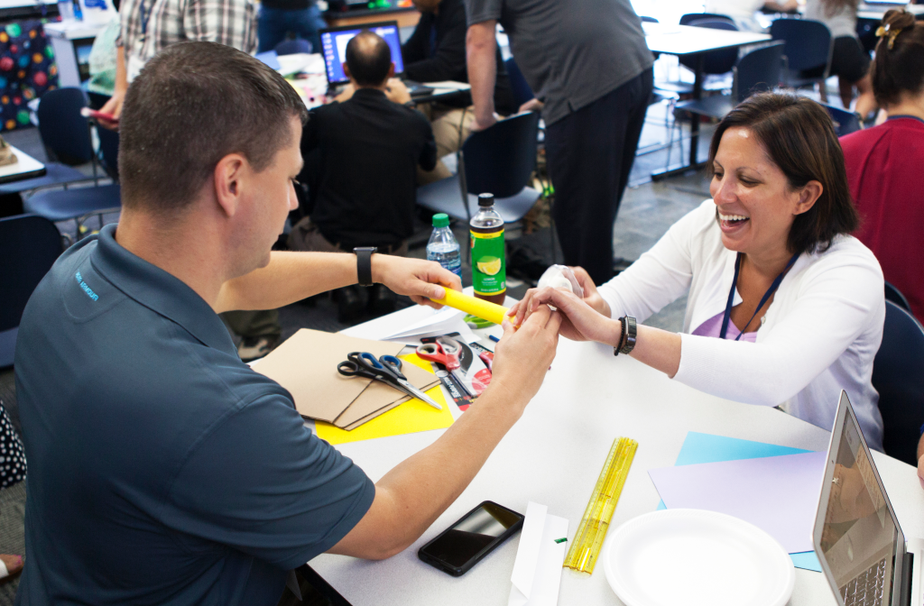 Two adults performing a small arts and crafts project over a table.