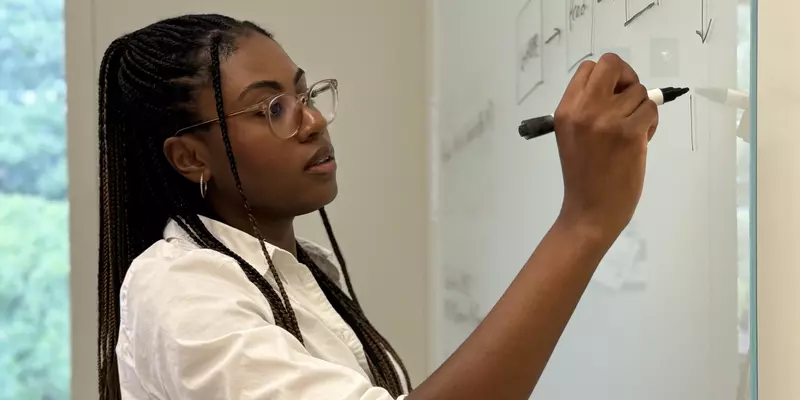 Ashley Hartwell, a researcher, stands in her office and writes concepts down on a glass board. 