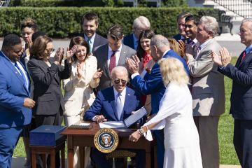 President Biden sits at a table with the recently signed 'CHIPS and Science Act,' surrounded by legislators and Vice President Kamala Harris.