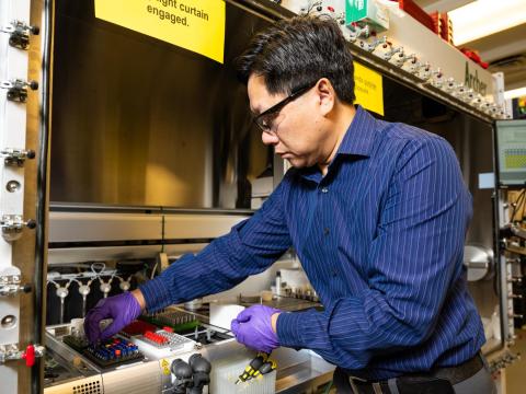 Photograph of a Wei Wang reaching into a fume hood