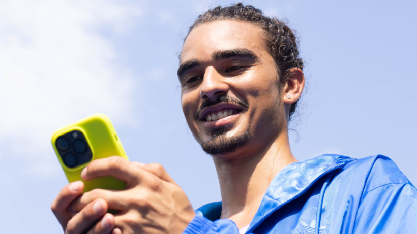 A man holding his phone, looking down at the screen and smiling.