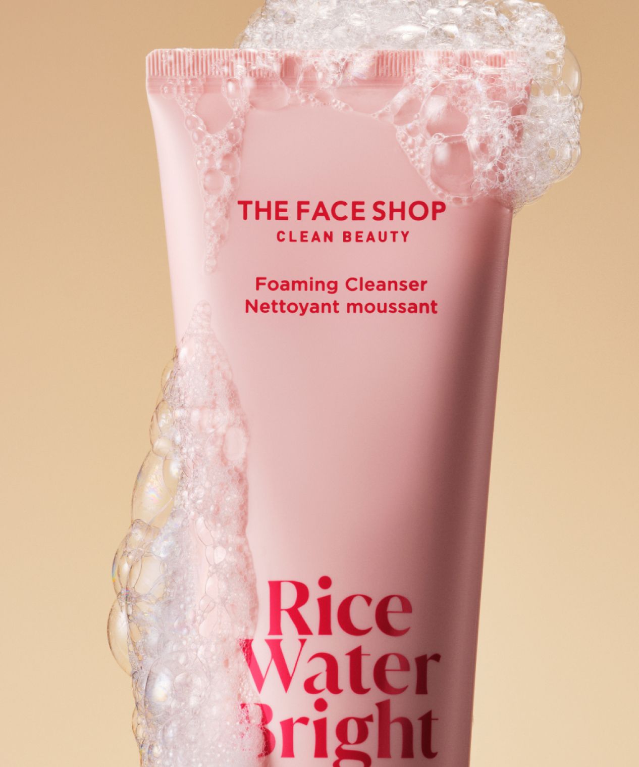 A tube of the face shop rice water bright cleansing foam covered in bubbles is displayed on a warm beige background.