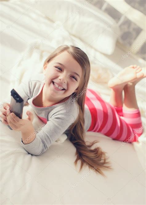 Little girl lying in bed with a remote control TV — Stock Photo ...