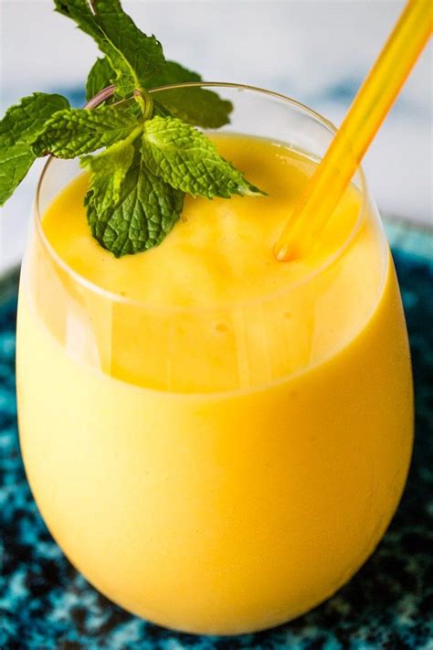 Mango milkshake in a glass with a sprig of mint and a yellow straw ...