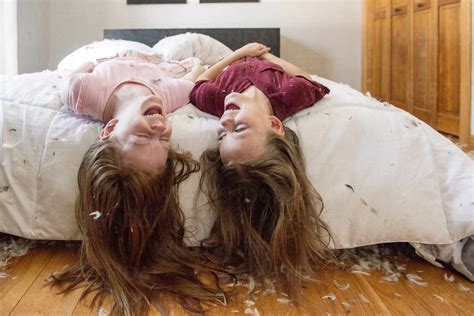 Two happy young girls having a feather pillow fight on the bed. stock photo