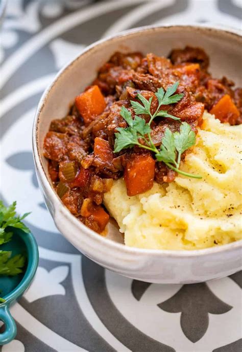 a white bowl filled with mashed potatoes and meat next to a green garnish