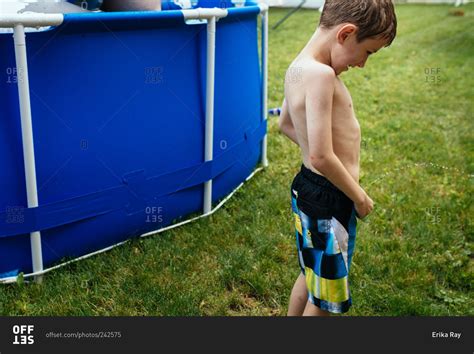 Little boy peeing by pool in backyard stock photo - OFFSET