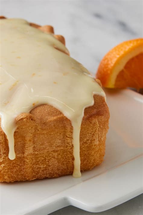 an orange cake with icing on a white plate next to some sliced oranges