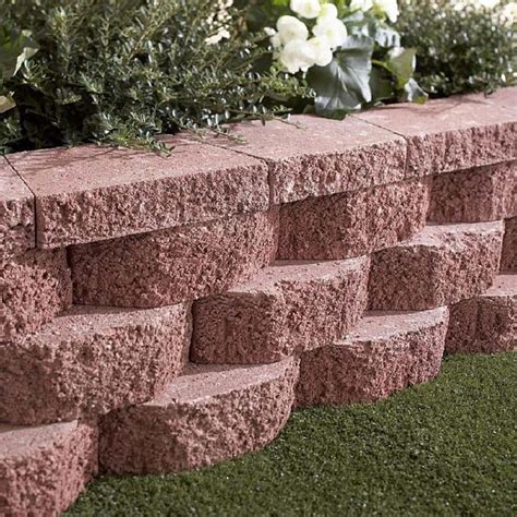 a close up of a brick wall with flowers in the background and grass on ...