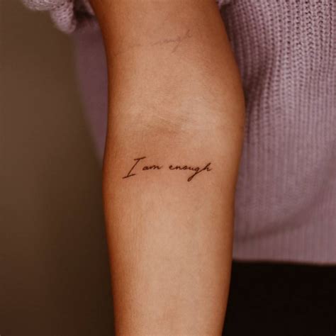 "I am enough" lettering tattoo on the inner forearm.