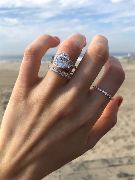 a woman's hand with two rings on it and the beach in the background