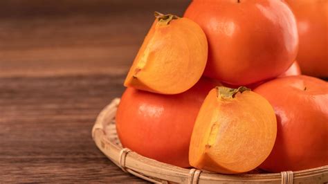 Fresh beautiful sliced sweet persimmon kaki on dark wooden table with ...