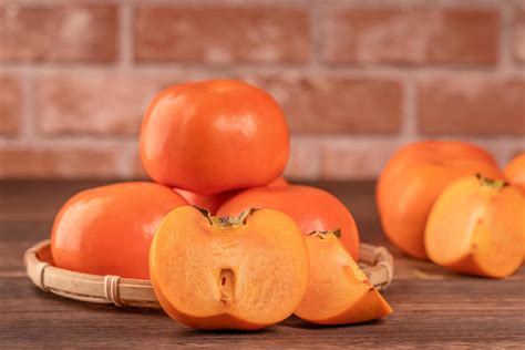 Sliced sweet persimmon kaki in a bamboo sieve basket on dark wooden ...