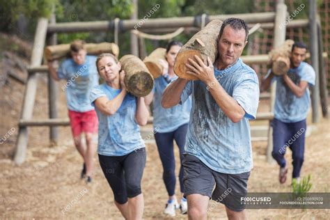 Determined people running with logs on boot camp obstacle course ...