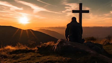 Silhouette of a man kneeling praying at the Cross of Jesus on a hill at ...