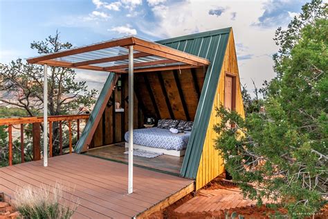 a small wooden cabin with a bed in the corner on a deck surrounded by trees