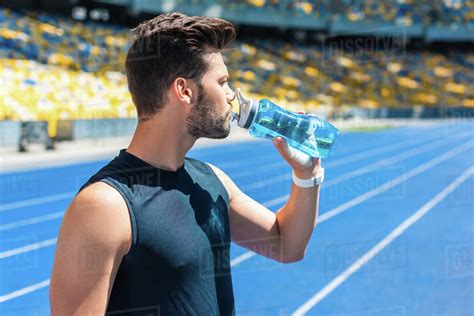 Attractive young man drinking water after training at sports stadium ...