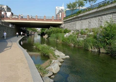 people are walking along the river under a bridge