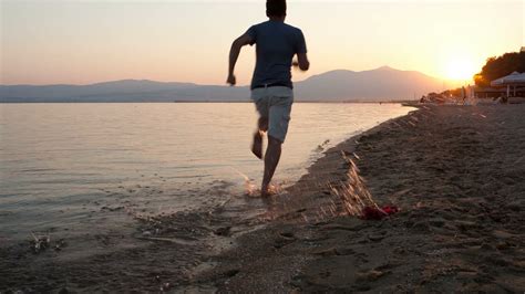 Man running away from the camera along a beach at the edge of the sea ...