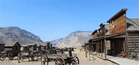 an old western town in the mountains with wooden buildings and wagons ...