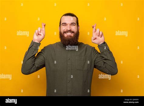 Young bearded man with exhilarated face is crossing fingers for a wish ...