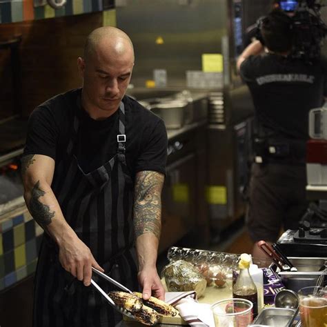 a man cooking food in a kitchen next to another man with tattoos on his arm