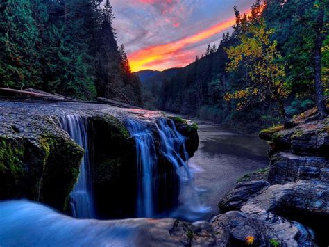 a waterfall in the middle of a forest at sunset