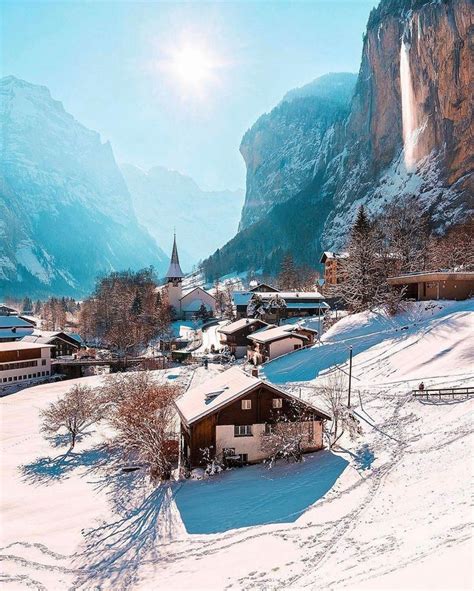 a snow covered village with mountains in the background and sun shining ...