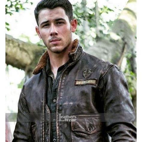 a man wearing a brown leather jacket standing in front of a tree