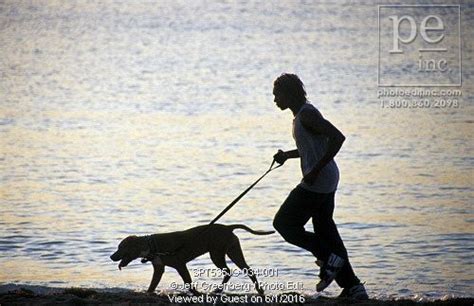 Black man running with his dog on leash silhouetted against ocean at ...