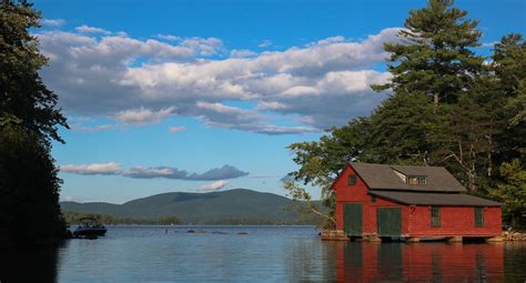 a red house sitting on top of a lake surrounded by trees and mountains ...