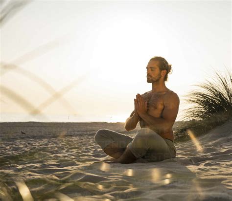 Shirtless young man meditating while practicing yoga sitting with hands ...