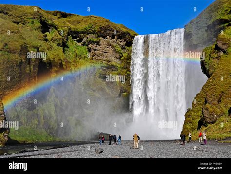 Skogafoss waterfall and rainbow with incidental tourists. Skogafoss is ...