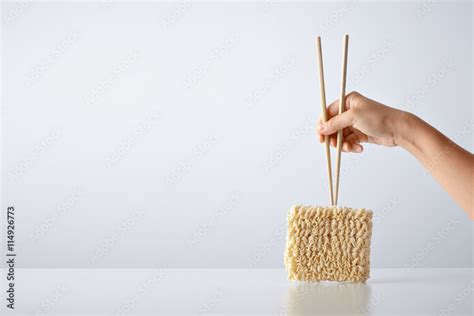 Hand with chopsticks above pack of pressed dry egg noodles isolated on ...