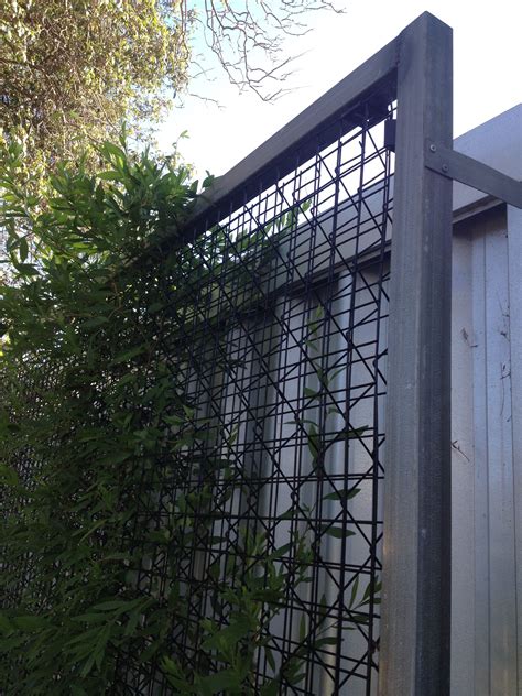 a metal fence with plants growing on it next to a building in the ...