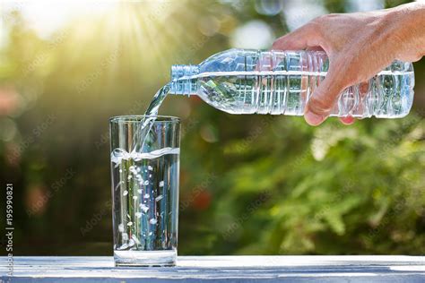 Hand holding drinking water bottle pouring water into glass on wooden ...