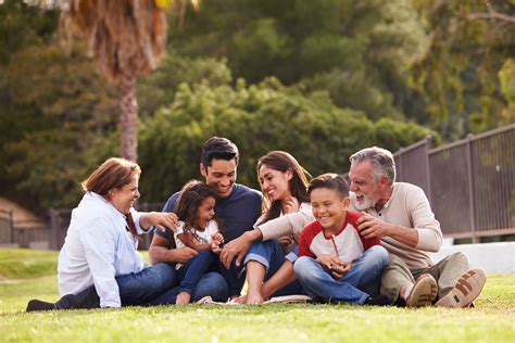 Happy three generation Hispanic family sitting on the grass toge ...