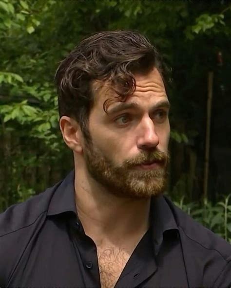 a man with a beard and black shirt in front of some green trees looking ...