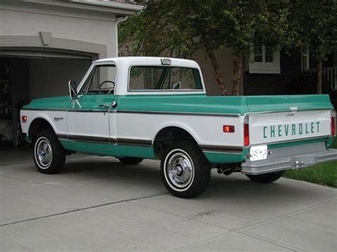 a green and white chevrolet truck parked in front of a garage with its ...