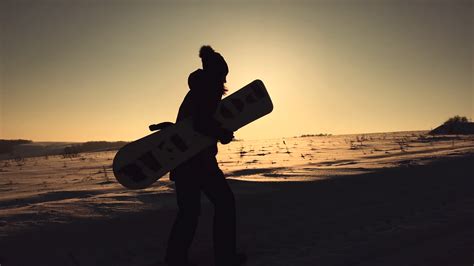 Silhouette girl snowboarder walk with snowboard on mountain top at ...